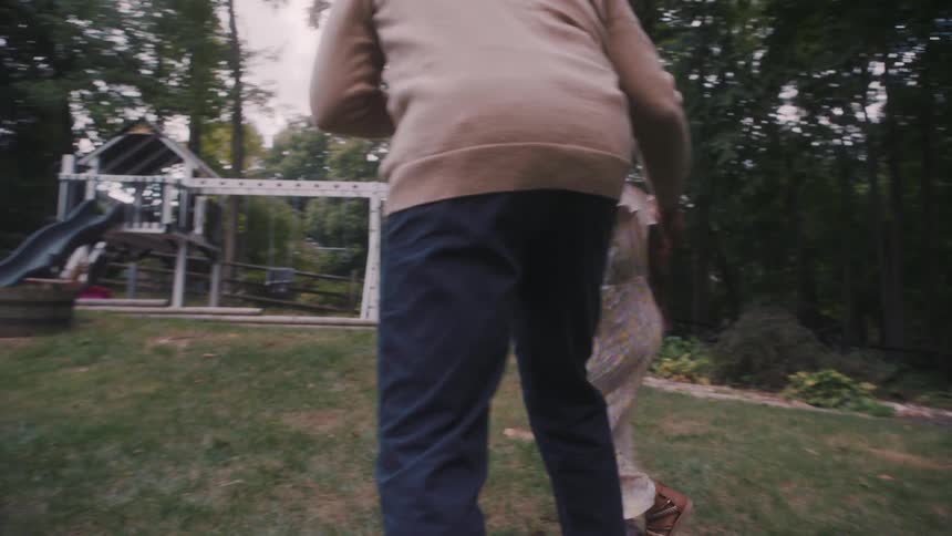 A father dances with his young daughter in a backyard