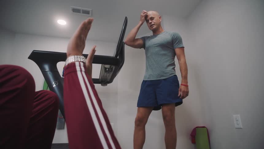 A man stretches on the floor on a mat while a personal trainer gives instructions