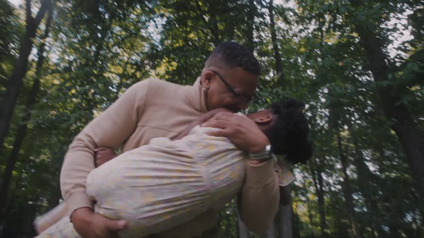 Father holding his daughter and playing while they are in a garden with trees