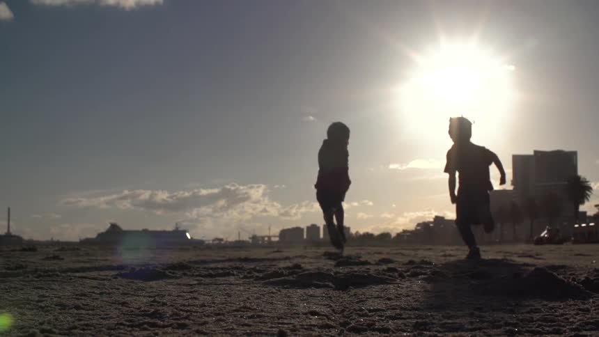 Two children running in the sand towards some buildings