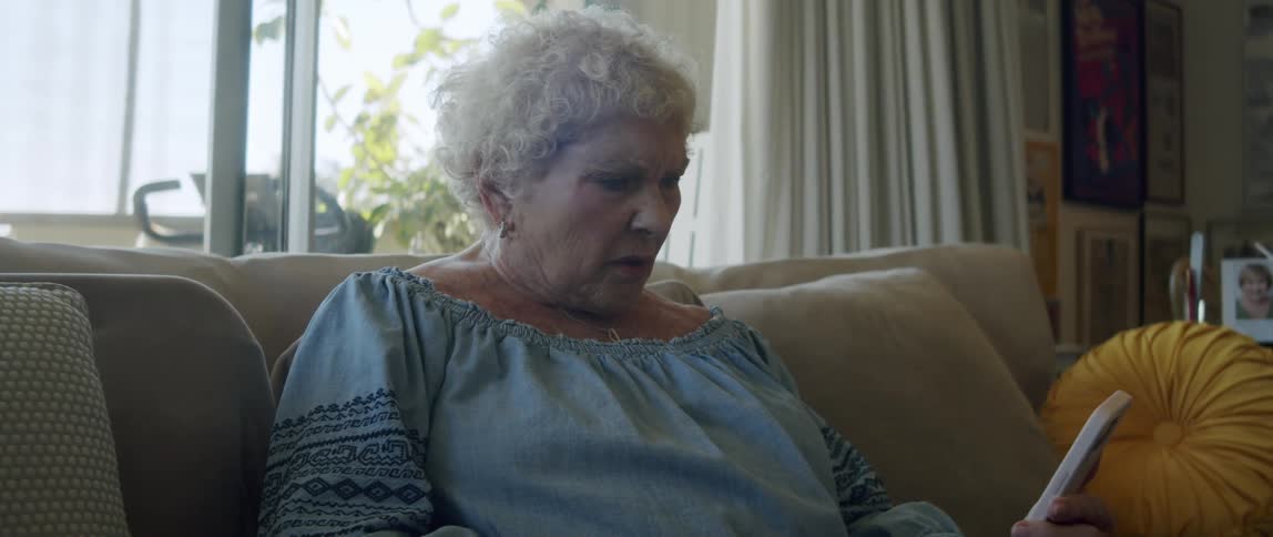 An elderly woman reading on her smartphone sitting on the couch at home