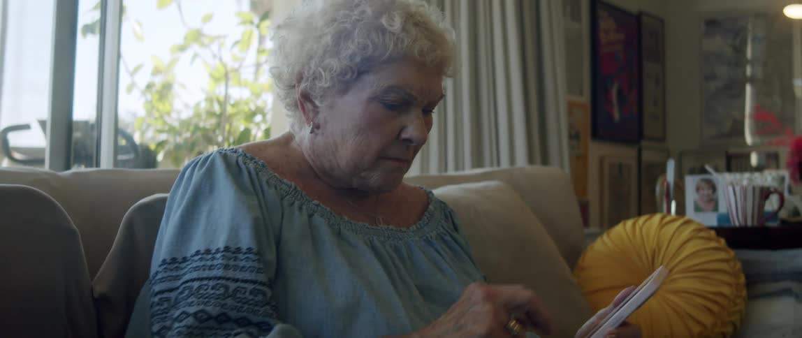 Elderly woman sitting on sofa interacting with smartphone