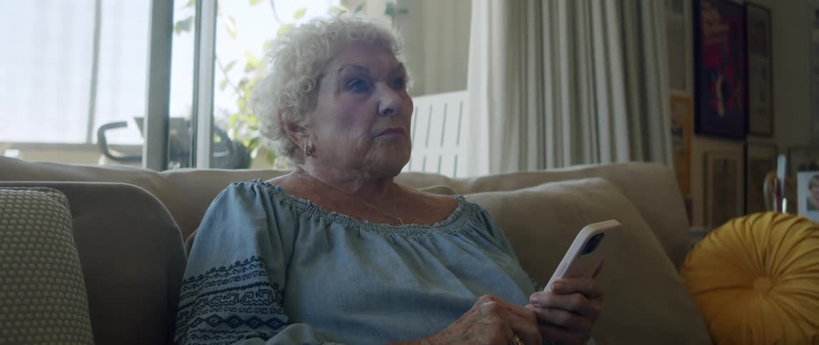 Elderly woman sitting on sofa typing on smartphone