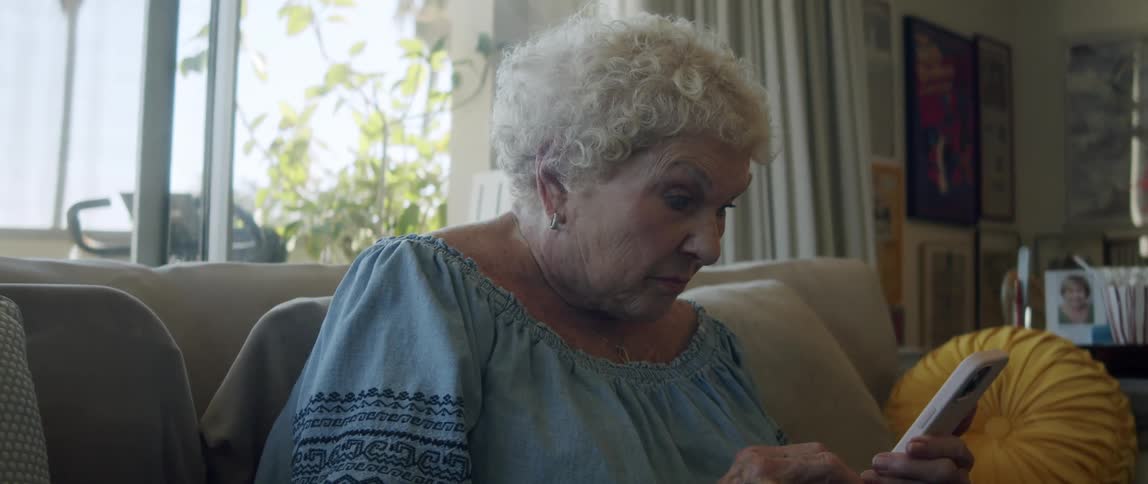 An elderly woman reading on her smartphone sitting on the couch at home