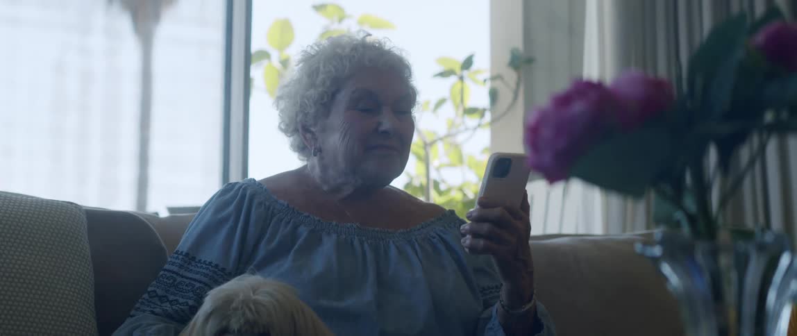 Elderly woman sitting in her living room with her dog sways while listening to music on her smartphone