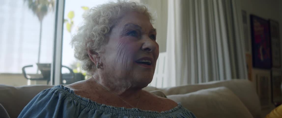 Elderly woman sitting on sofa in living room with happy facial expression and using smartphone