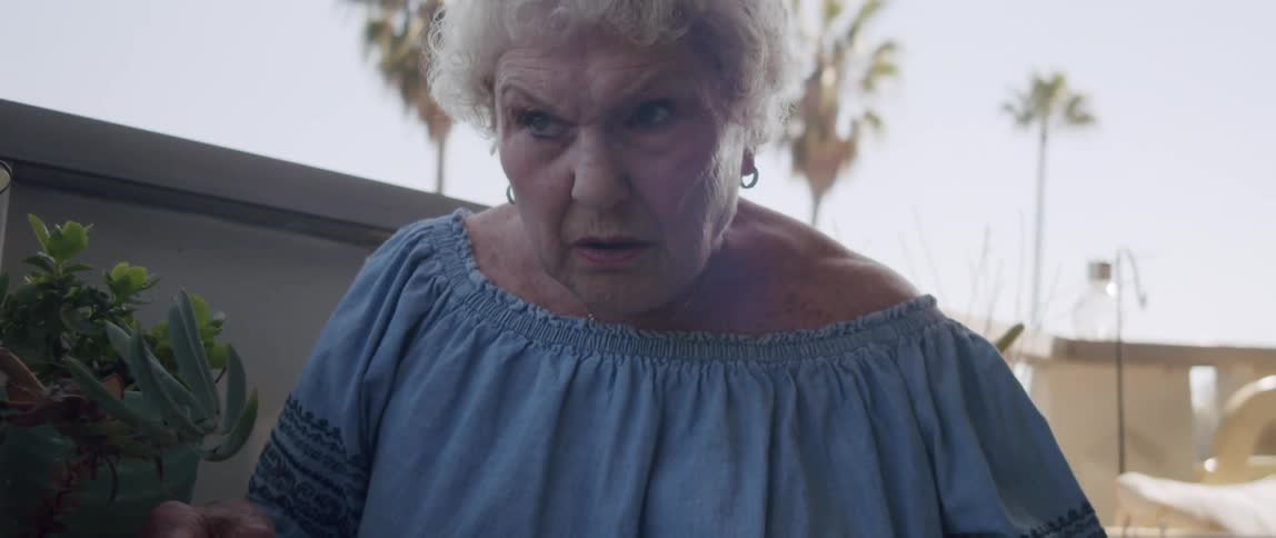 An elderly woman reading a newspaper on the porch or balcony