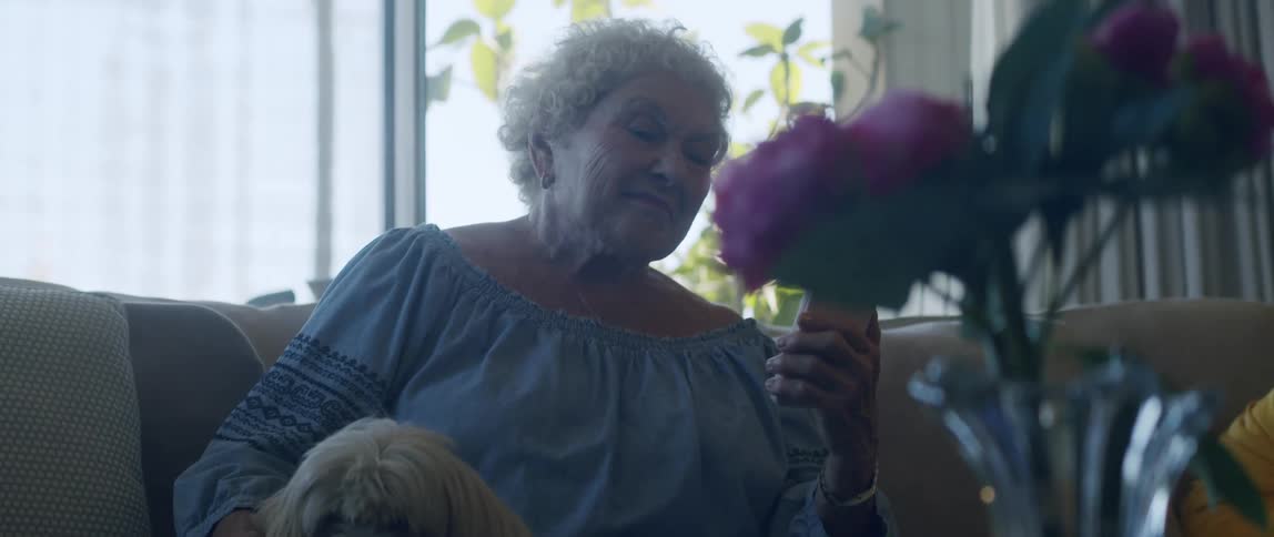 Elderly woman sitting in living room interacting with a smartphone and a dog by her side