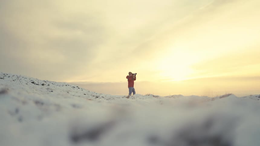 A photographer takes pictures on a snowy hillside at sunrise