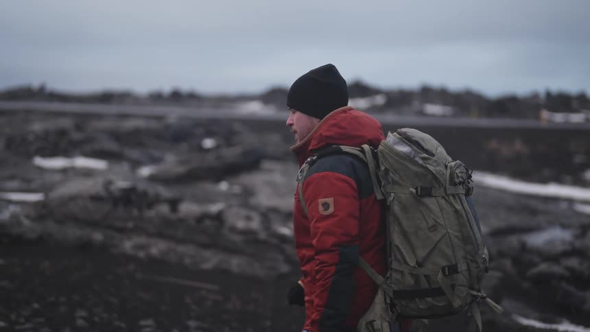 A photographer hikes through the snowy wilderness beneath an overcast sky