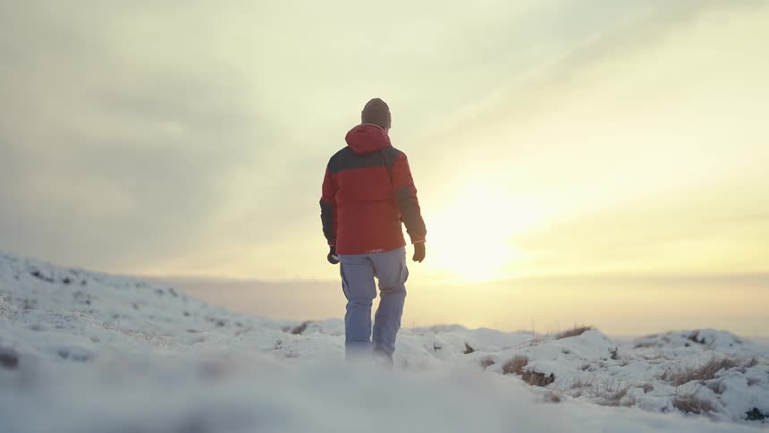 Man in red jacket walking on a snowy mountain by the sea and carrying a professional camera