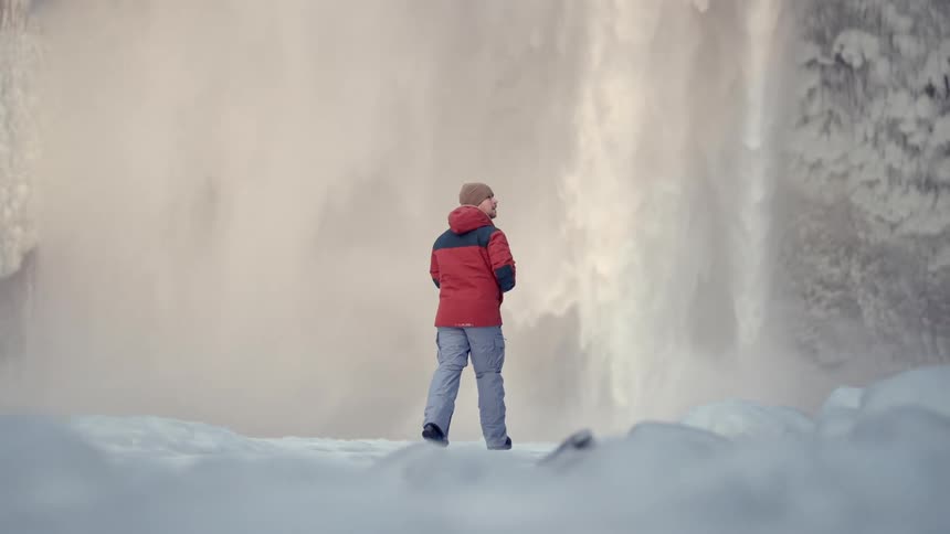 Photographer walking across snow in the forest towards a rapidly flowing waterfall