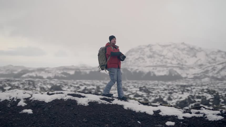 Man walking on a rock in a snowy mountain environment and using a professional camera