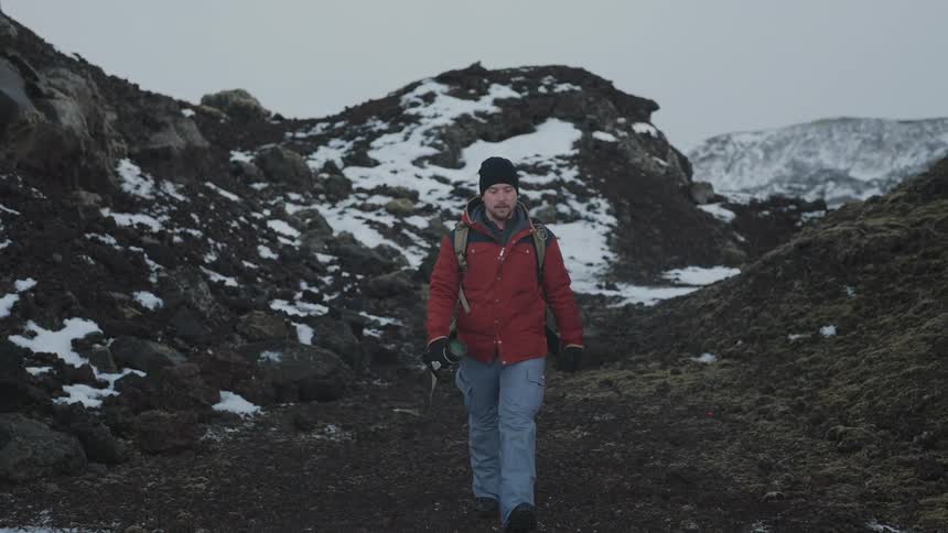 A man wearing winter clothes and a backpack hikes on a mountain pass