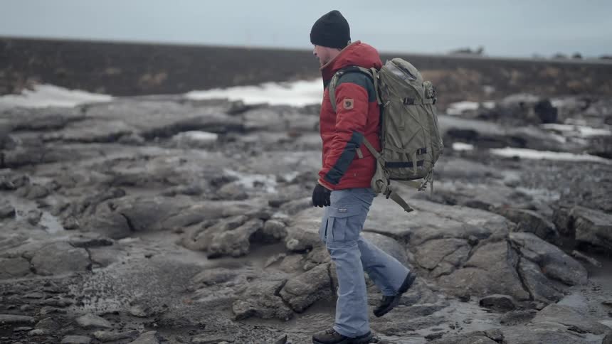 Man with backpack walking among rocks with a body of water in the background