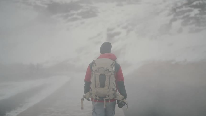 A man wearing a red jacket and carrying a large backpack walks along a misty snowcovered path