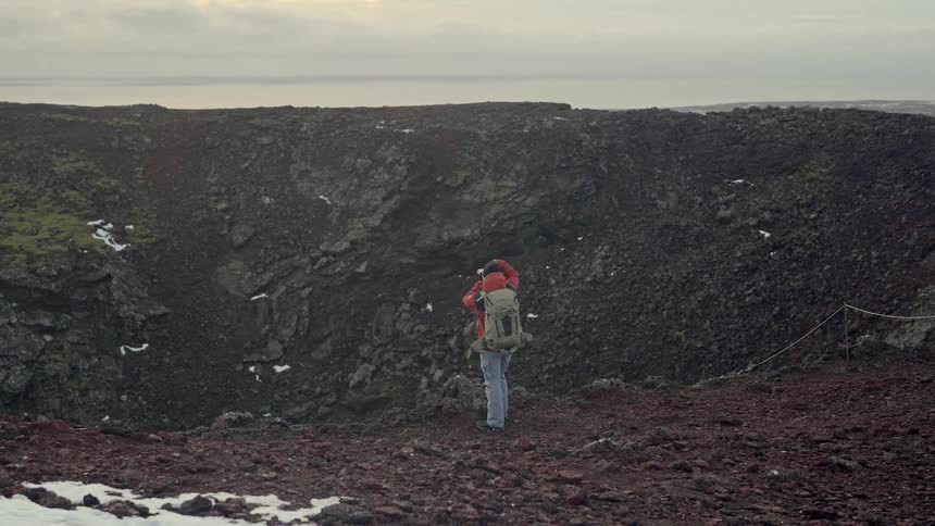 Man with a professional camera photographing a crater with the sea in the background