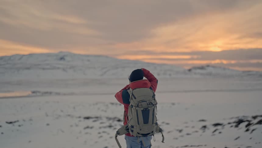 Photographer photographing a snowy natural area with mountains and an orangetoned sky