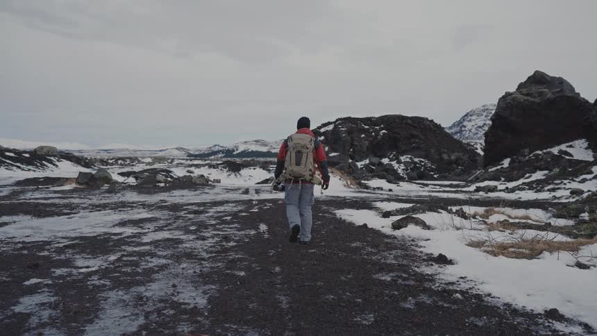 Natural landscape and a man with a backpack holding a professional camera walking through the snowy environment