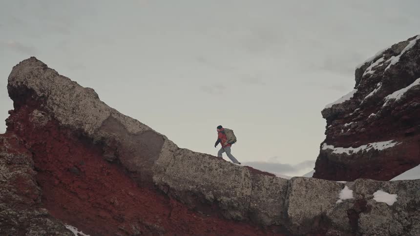 Man climbing a steep rocky slope against a cloudy sky