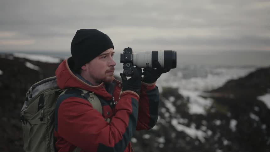 Man using a professional camera with zoom lens while standing on a snowy hill