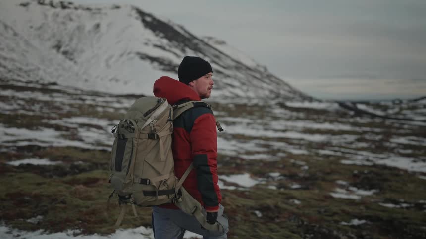 A photographer hikes through the snowy wilderness beneath an overcast sky
