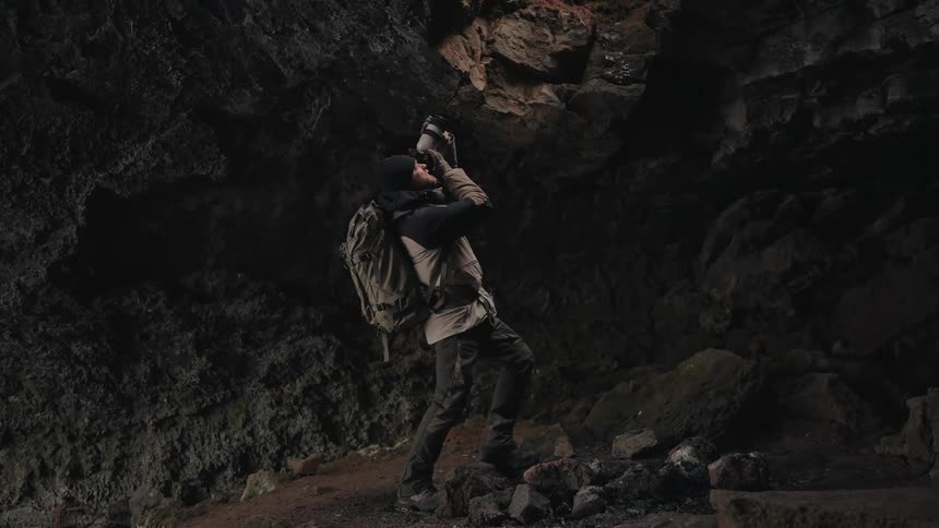 Photographer using a professional camera in a cave towards a hole at the top