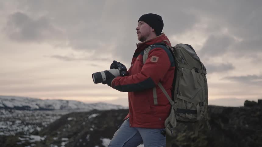 A man carrying a camera hikes up a mountain to take a photo