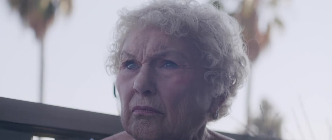 Elderly woman sitting outdoors frowns in reaction to what she reads in the newspaper