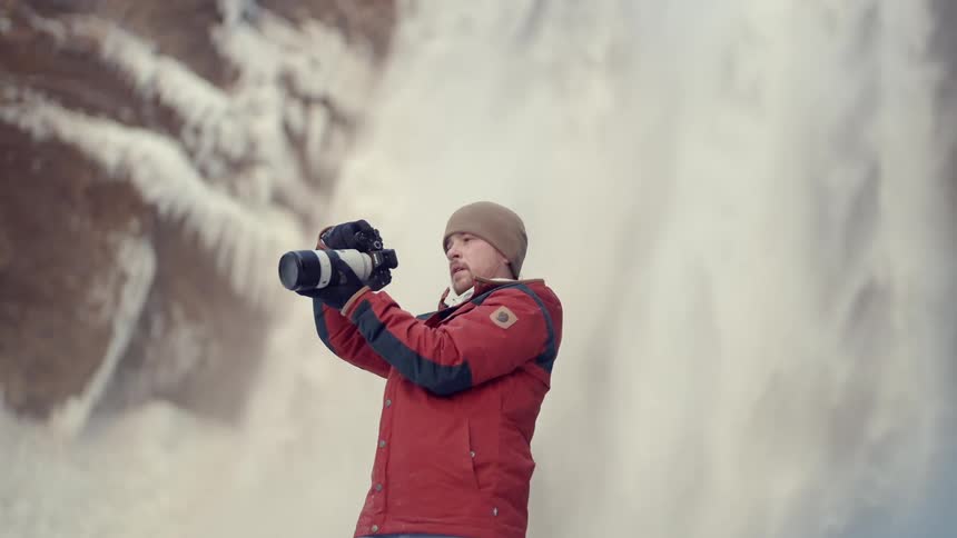 A photographer stands in front of a waterfall taking pictures