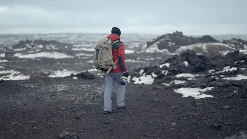 Man holding a camera with a professional lens walking through a snowy landscape on a cloudy day