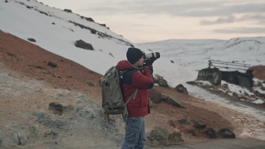 A photographer takes pictures of snowy mountains at sunset