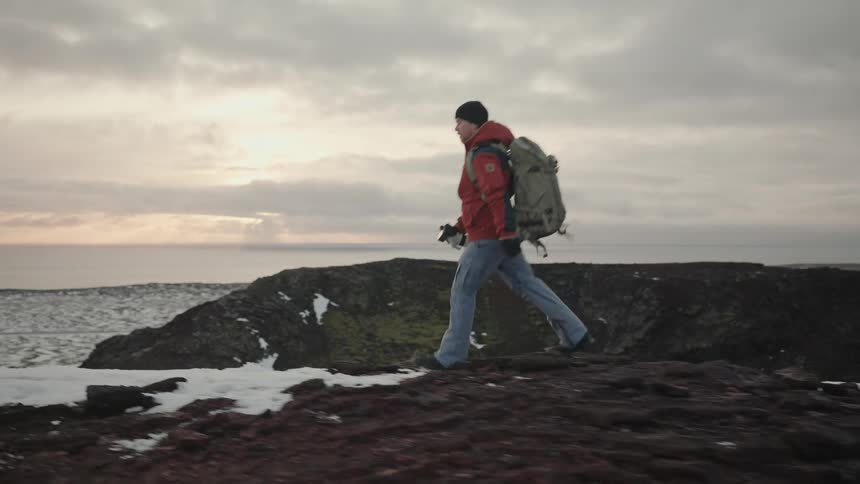 Man with backpack and professional camera walking on a snowy mountain on a cloudy morning