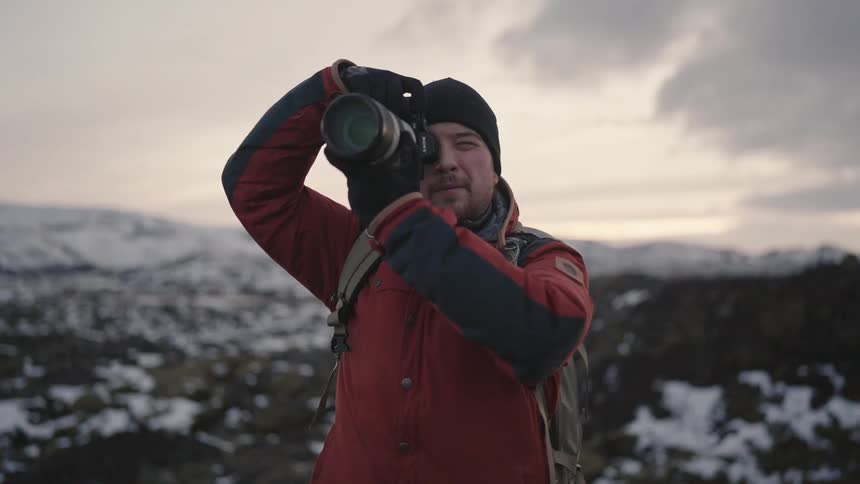 Male photographer hiking across rough snowy terrain stops to take a picture