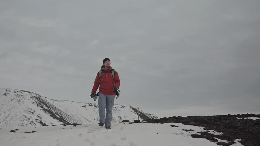 A photographer hikes through the snowy wilderness beneath an overcast sky