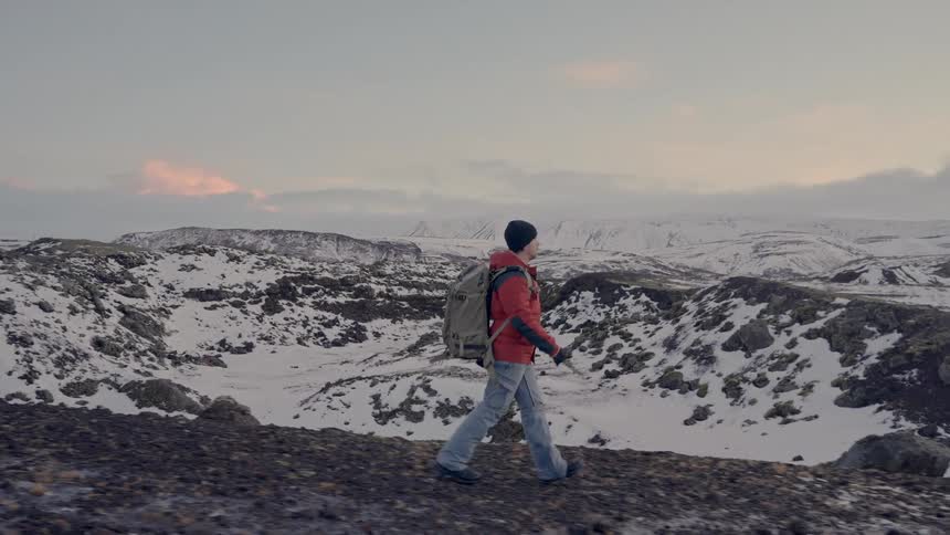 A photographer hikes through the snowy wilderness beneath an overcast sky