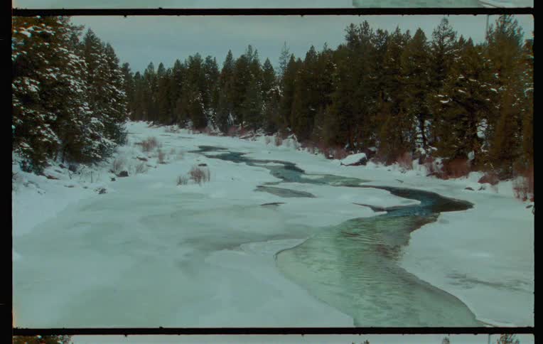 A partially frozen river runs through a forested area