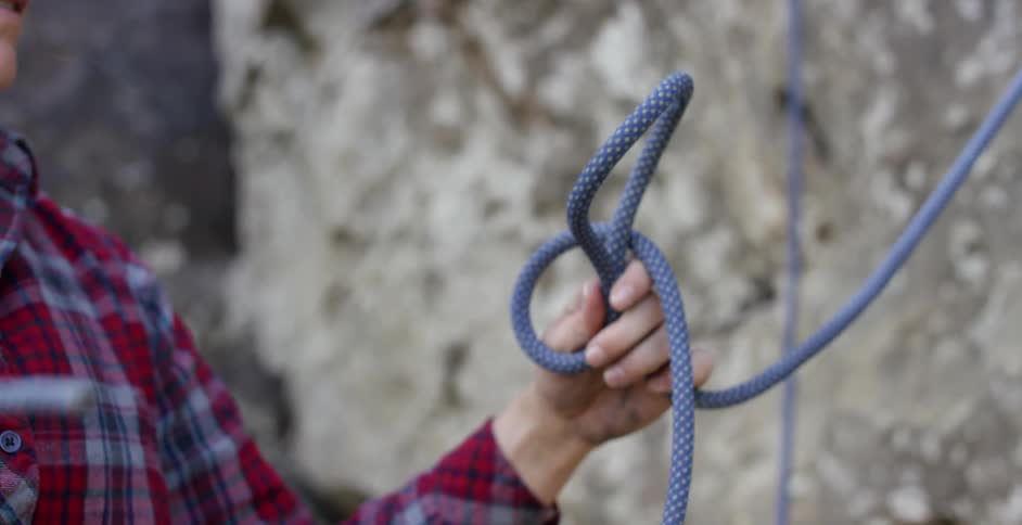 A person knots a rope at the base of a rock face