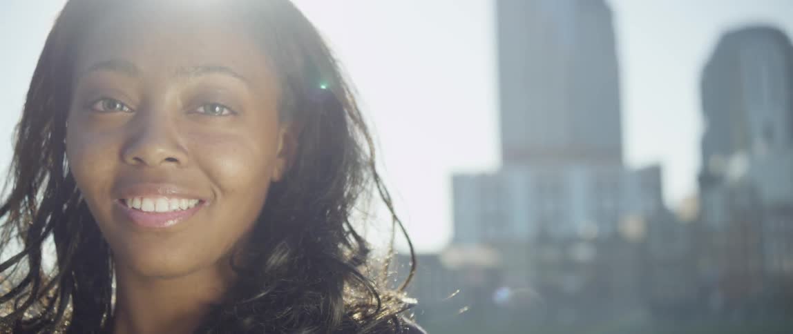 Woman smiles with buildings behind her on a sunny day