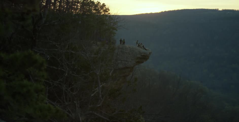 A group of people on a cliff over a forest at sunset