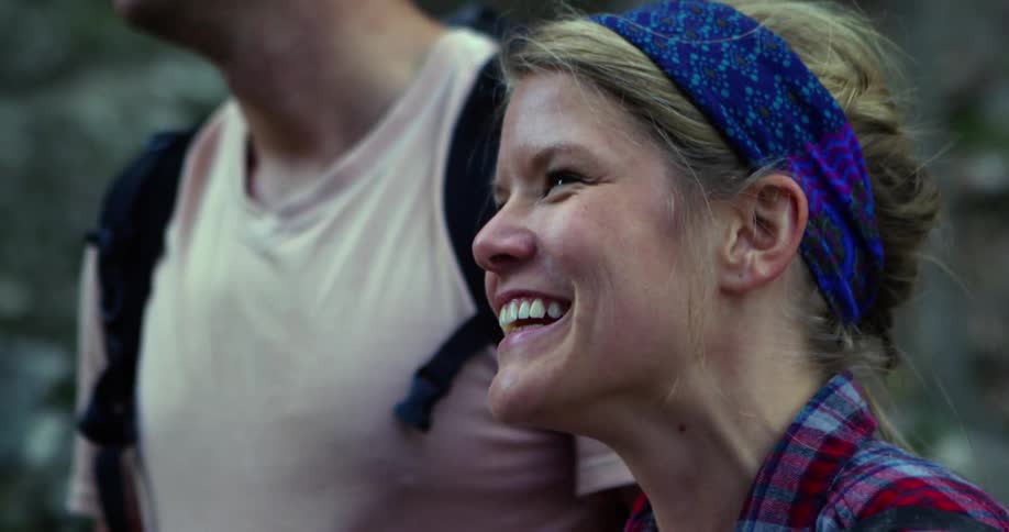 Blonde woman with a blue headband laughing hysterically in the wilderness amongst other people