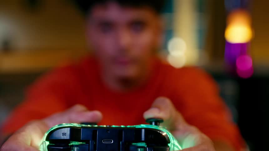 A boy in an orange shirt holding a video game controller with the focus on the controller in the foreground while the person is blurred in the background