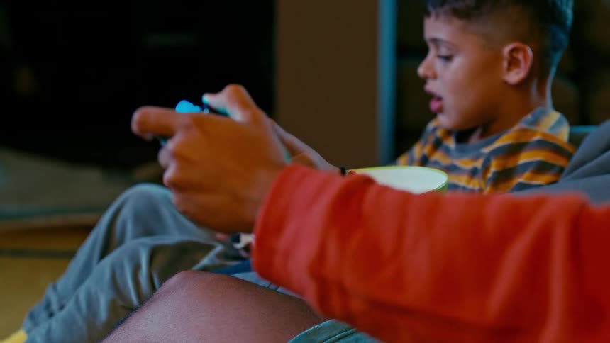 A person plays a videogame as his little brother sits next to him with a bowl of popcorn