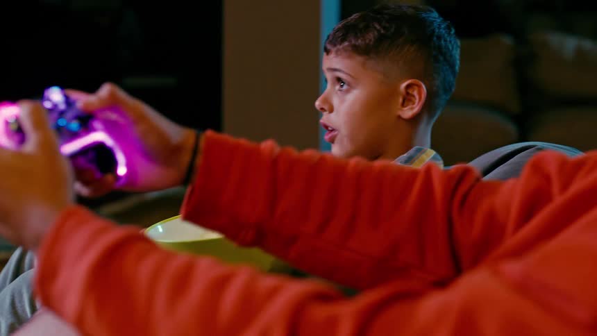Father uses a controller to play a game while his son talks while he watches
