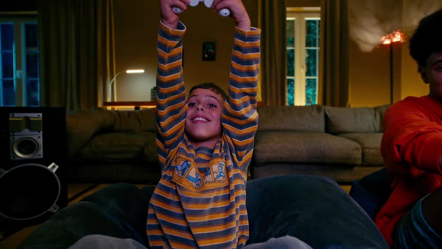 Teenager and a child playing video games together and having fun in the living room at night