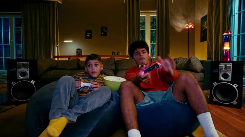 Boys sitting eating popcorn and playing video games in living room at night