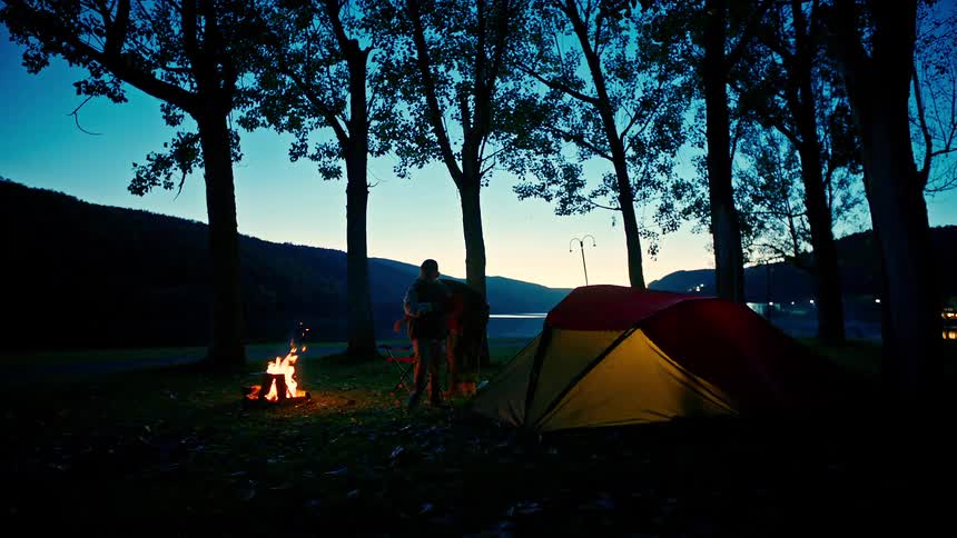 Two young people arranging chairs next to a campfire at a campsite
