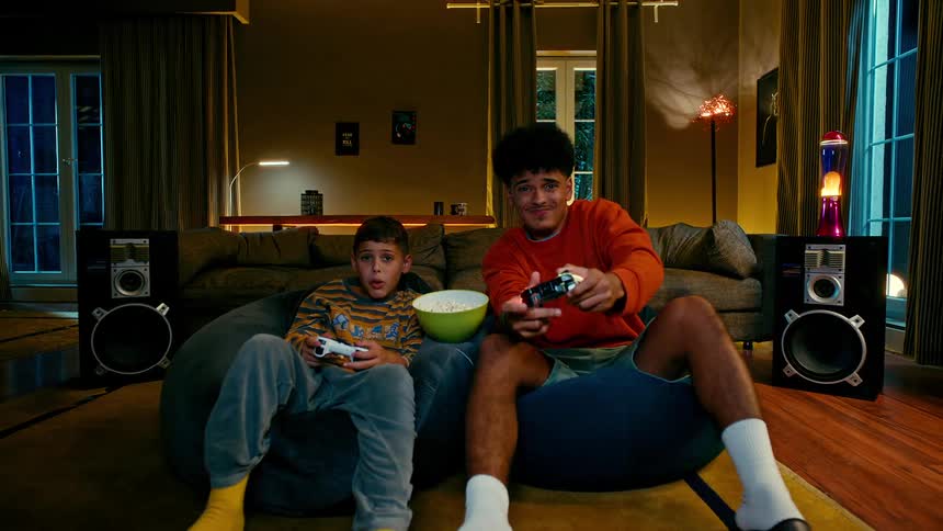 Teenage girl and a boy playing video games together while sitting in the living room at night