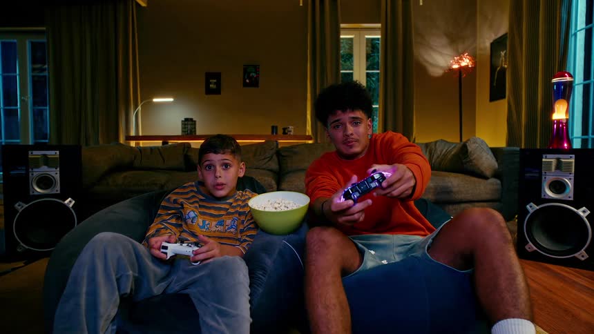 A young boy and an older boy sit in beanbag chairs intensely focused on playing video games