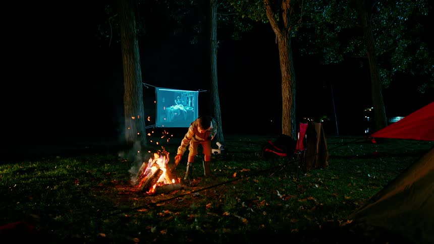 Child holds stick in a campfire until it starts burning then swings it around at night